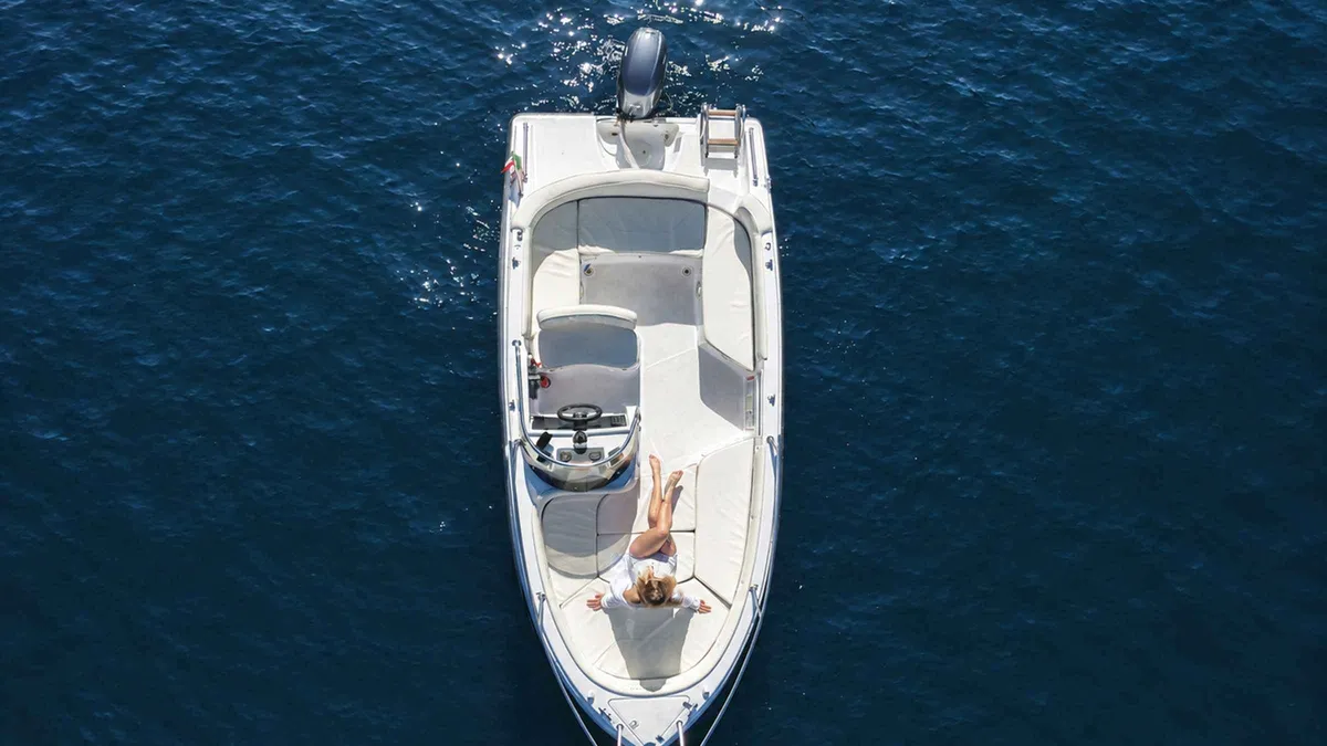 A couple steering a small rental boat away from the Como pier on a self-drive boat rental in Como, Italy